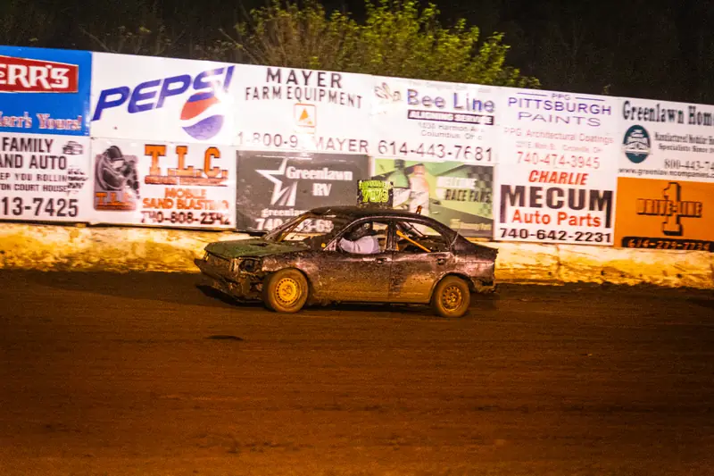 Lit backstretch billboard wall behind a race car at night