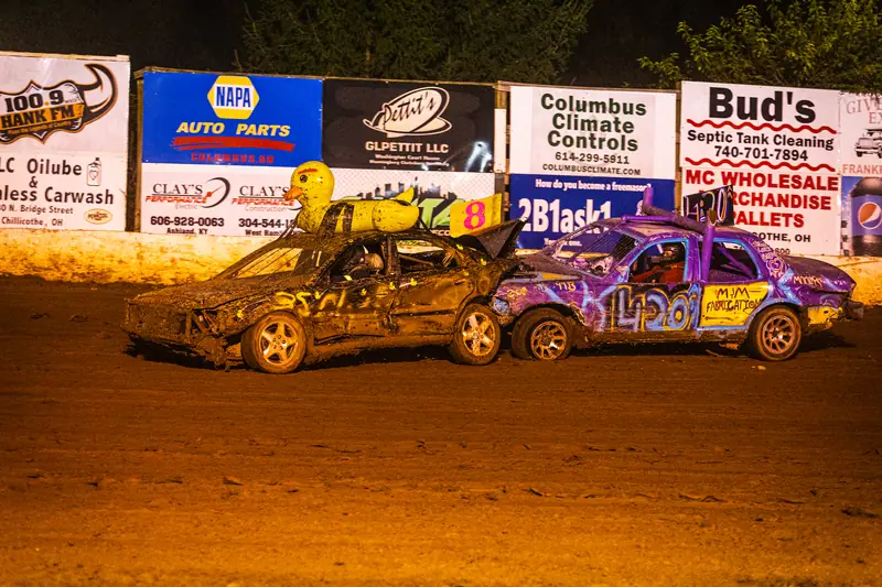 Two cars racing in front of a row of sponsor billboards